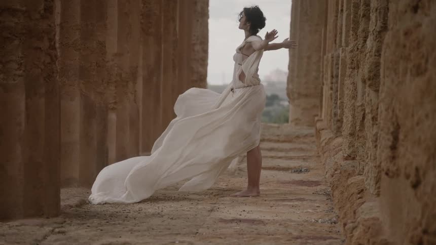 Woman stands with outstretched arms as her dress billows in the breeze