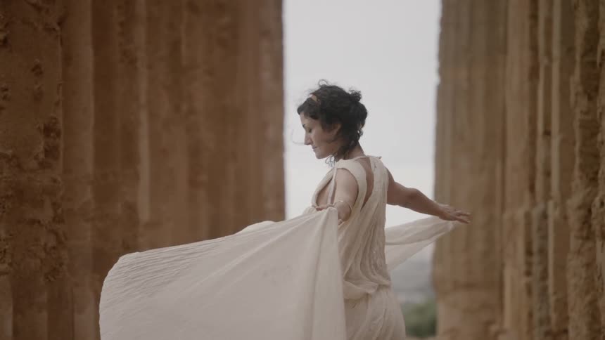 A woman holding the train of her dress up as it billows in the wind