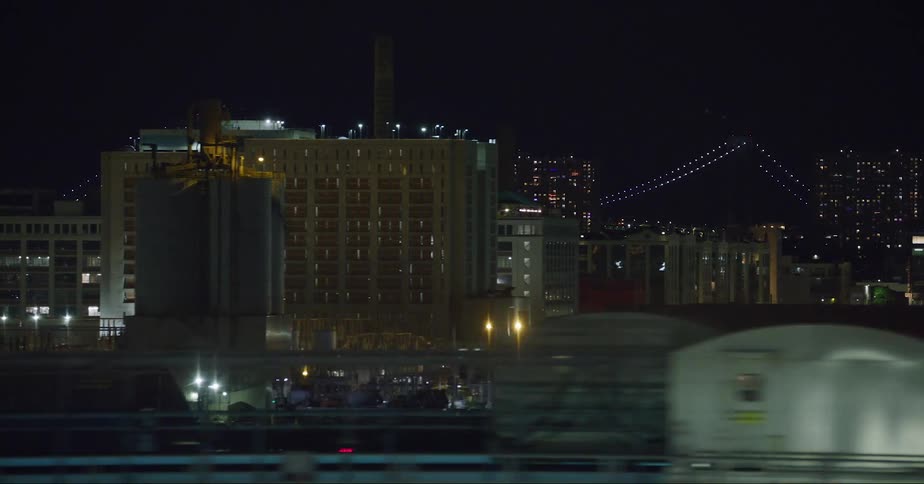 Downtown buildings in the city are lit up at night and lights on a suspension bridge glow in the sky