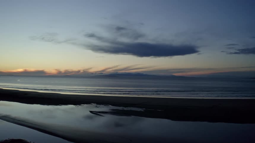 The sun is setting in the horizon of the beach reflecting colourful sky
