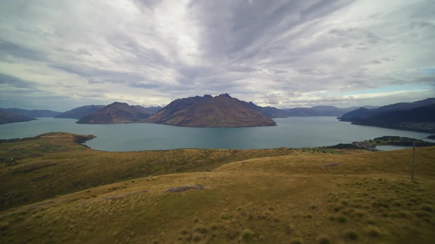 Aerial view of brown native grass hill overlooking calm lake and distant mountains