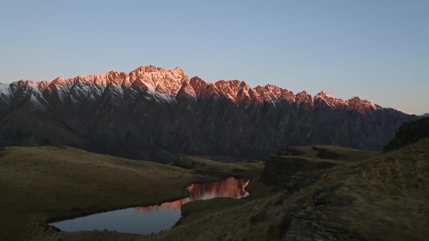 Aerial view of golden snow covered mountains reflecting in alpine lake is displayed at dusk