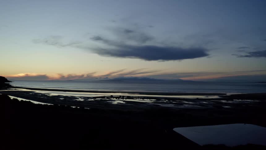 Aerial view of the dark contour of a beach next to the ocean at evening