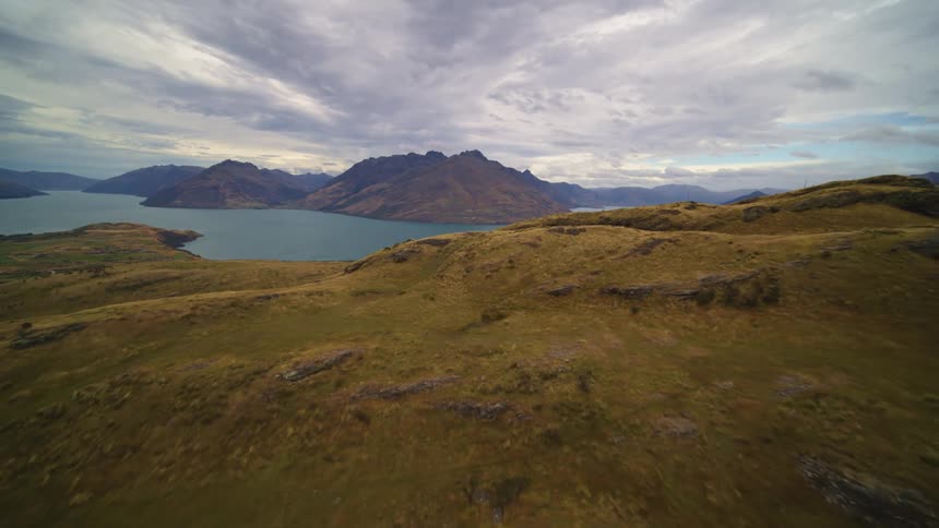 Rocks are scattered on grass covered hills and mountains are in the distance under a cloudy sky