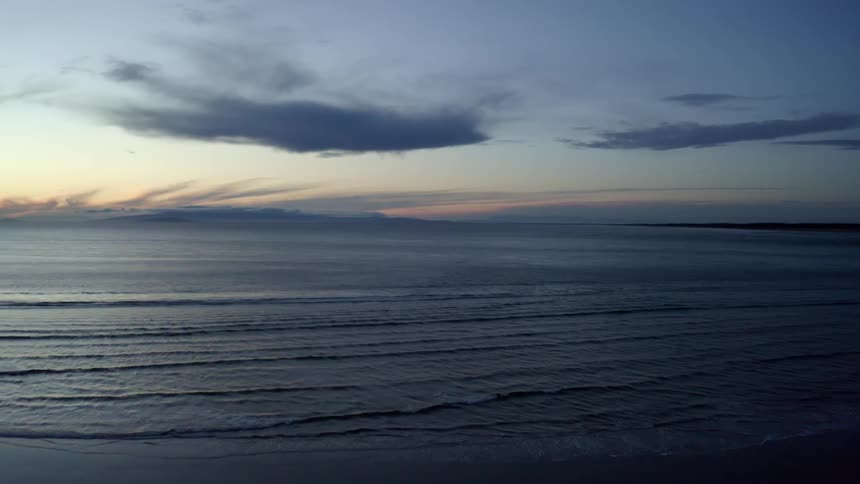 An aerial view of calm waves rolling in the ocean and on to the shore