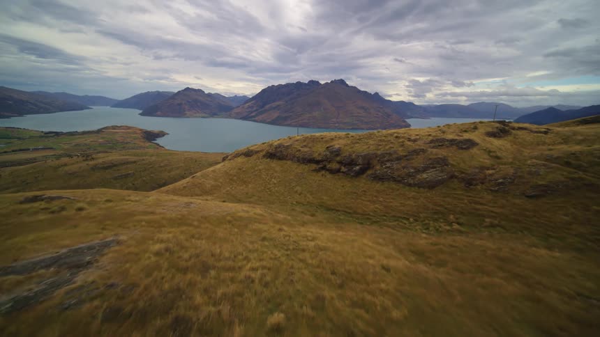 Low level aerial over grassland towards calm lake a cloudy daytime sky