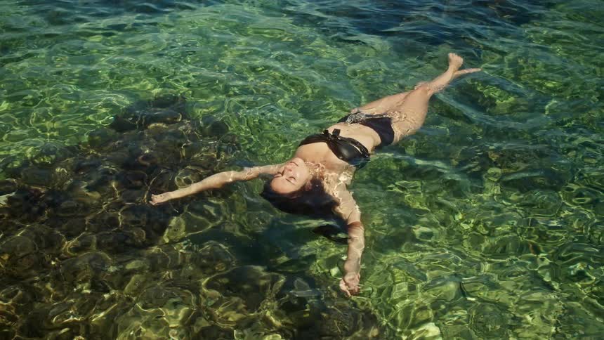 Woman in black bikini lies in sea water