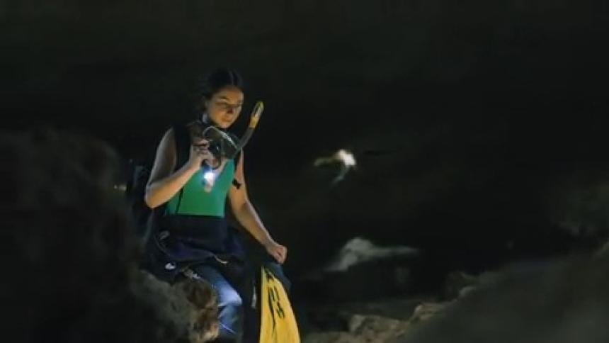 A woman is exploring a cave with a flash light