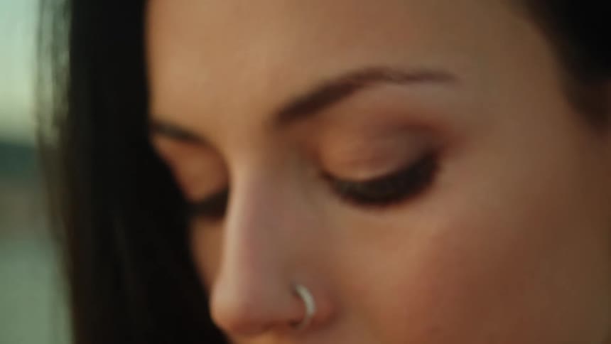 A woman wearing a silver nose ring is looking around as she has her hand on her earring