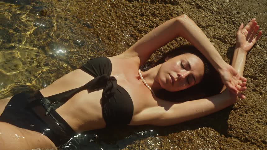 A woman is laying on the beach in the ocean