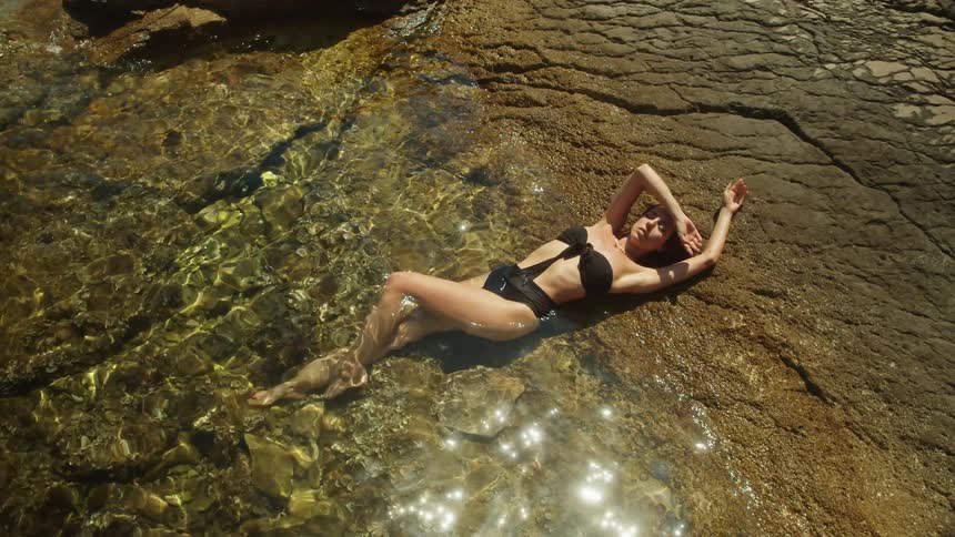 Woman in black bikini lies on seaside on the coast