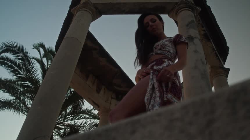 A woman poses in a gazebo pushing her skirt slit open hand on her thigh