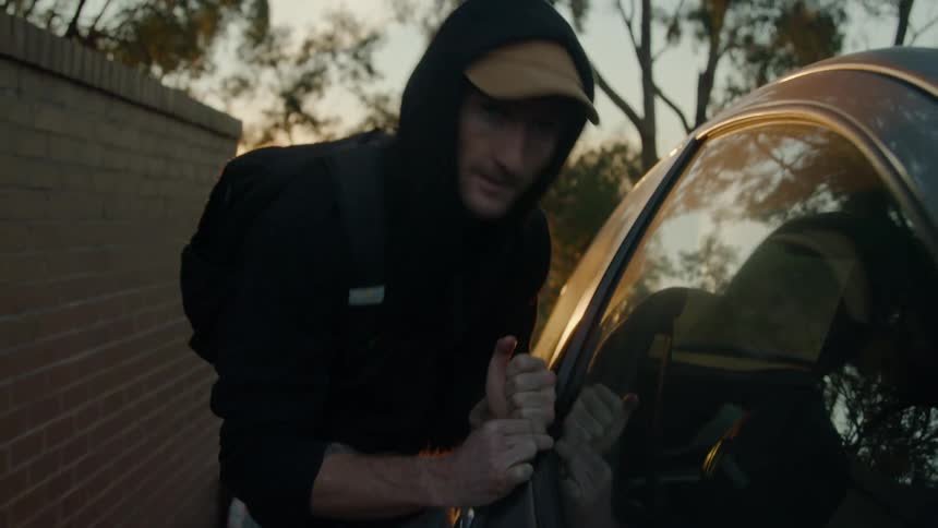 Man with black hoodie backpack and jeans breaks into car using poker at dusk
