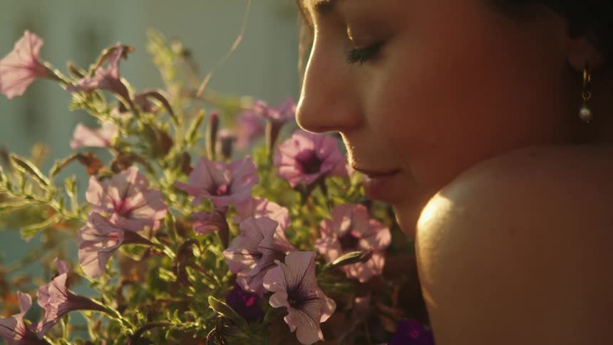 A woman is outdoors and is smelling flowers