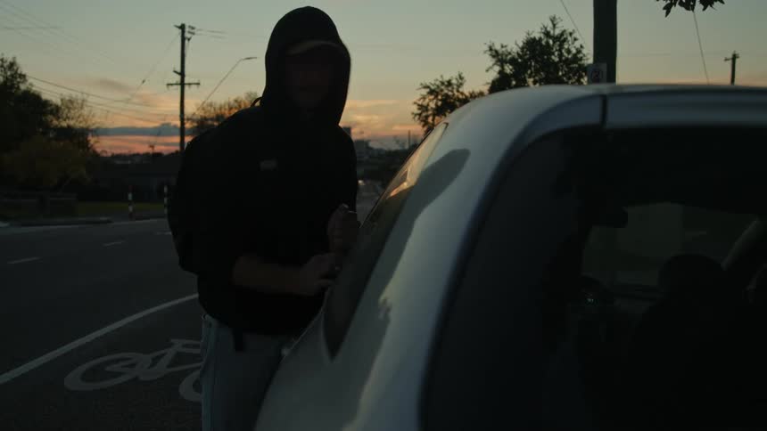 Man with black hoodie backpack and jeans breaks into white car using poker