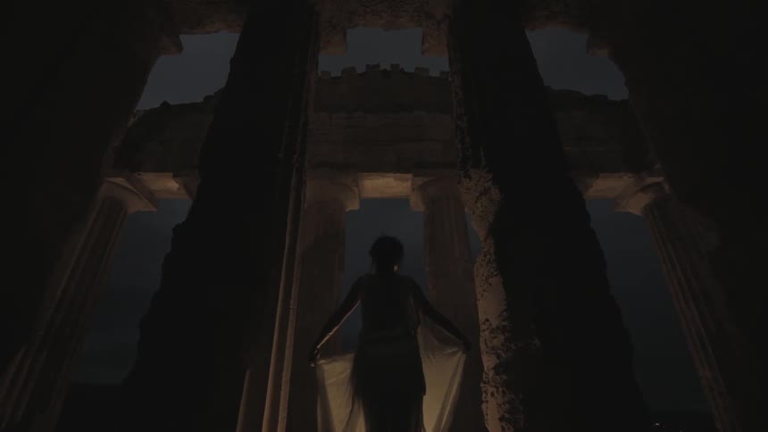 A woman standing between columns at the acropolis as night falls