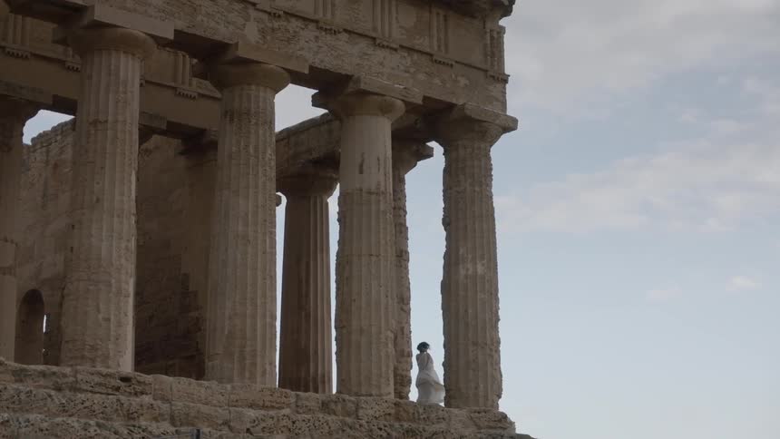 A woman stands up near some very large pillars