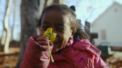 A girl smiles while smelling a flower
