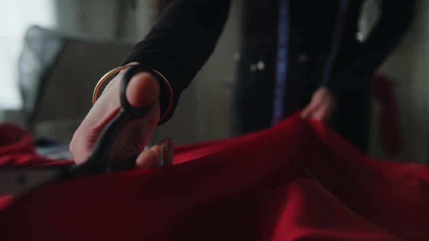 A woman is cutting a large red piece of fabric on a table