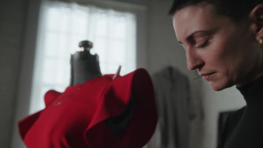 A woman is standing next to a mannequin pinning fabric on clothes she is making