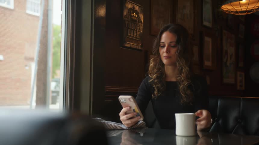 A woman is using her phone as she drinks coffee