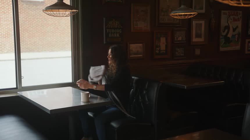A woman is at a restaurant and gets into a booth by herself with a mug and purse in her hand