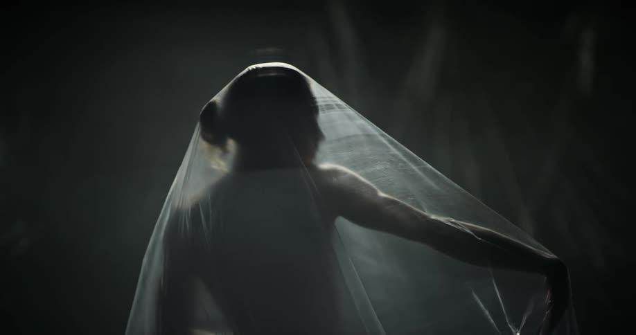 Topless woman with brown hair moves under plastic bag in studio