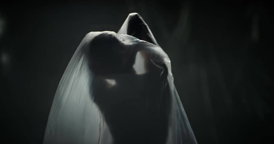 A naked woman under plastic wrap stretches her arms and tries to remove the plastic