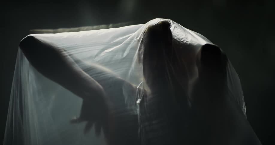 A woman slowly moving her arms under a translucent plastic bag in front of a dark background