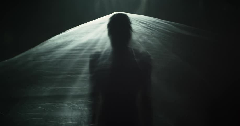 Silhouette of a woman sitting under a translucent plastic bag in front of a dark background
