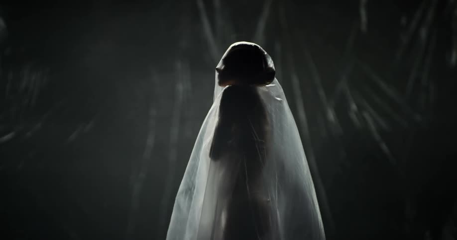 A nude woman is standing under sheer fabric with her arms crossed and hands on her shoulders and she looks up