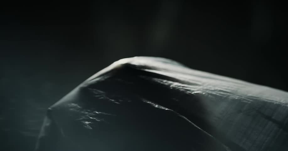 A woman looks up under a translucent plastic bag in front of a dark background