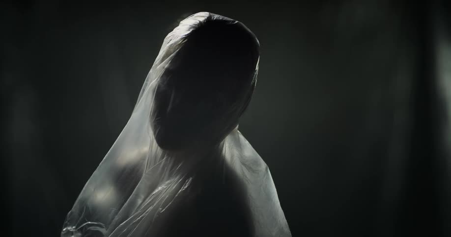 A woman covered in plastic turns and lifts her head upwards