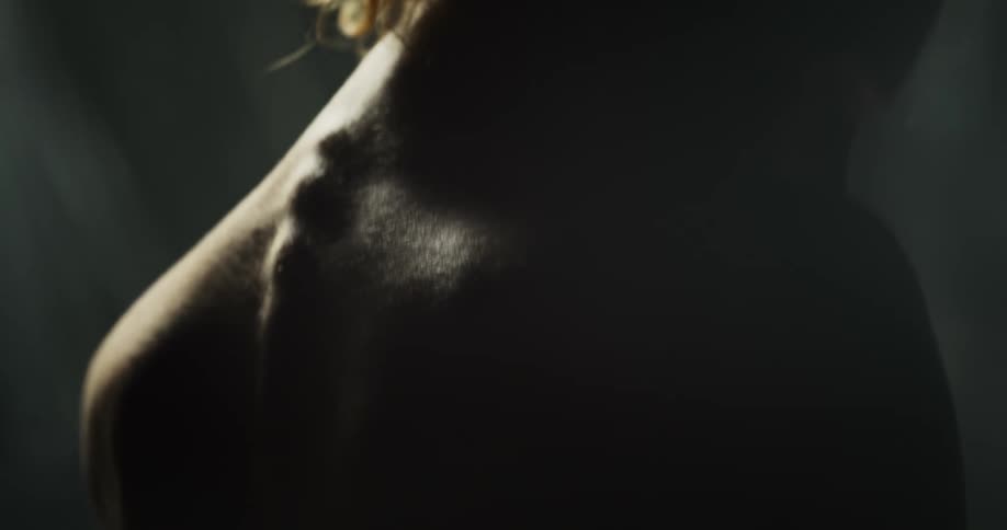 Naked woman looks over her right shoulder while the sun shines on her spine