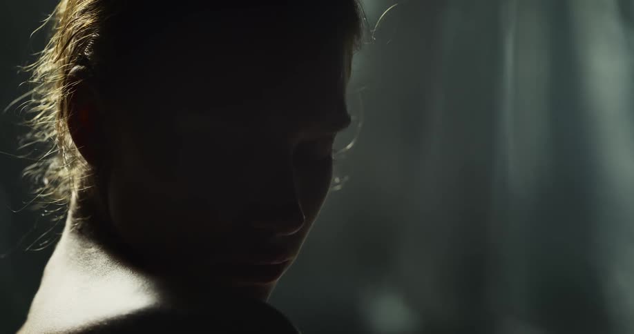 A woman is covered in darkness as she looks to the side