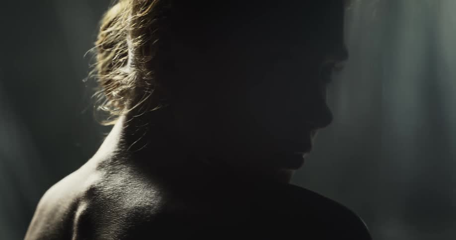 Naked woman looks over her right shoulder while the sun shines on her spine