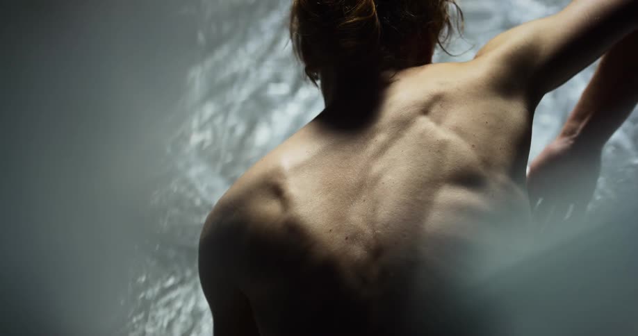 A womans back bones protrude as she flexes and moves her arms