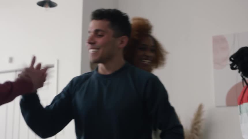 A man and woman sitting on a sofa in the living room of a house rise to happily greet a group of people with hugs