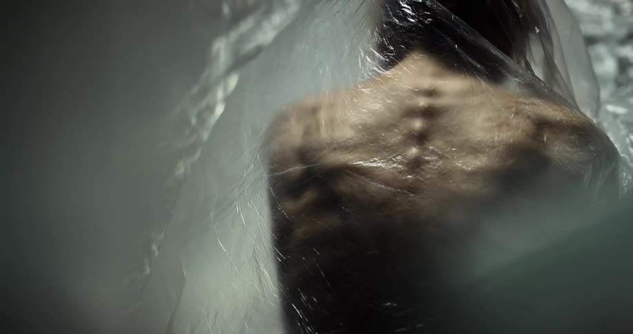 Bones protrude from a thin womans back as she sits under a plastic tarp