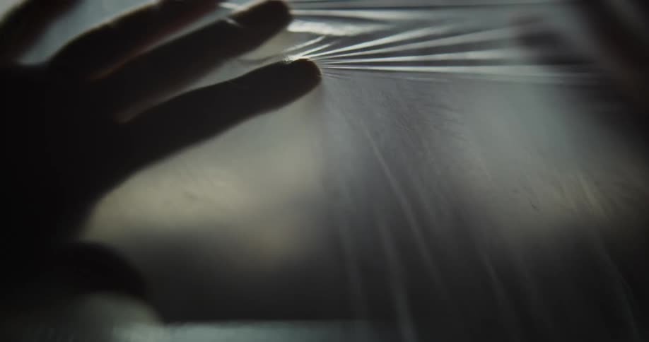 Someones hands are shown underneath a plastic sheet pressing their palms against it in front of them