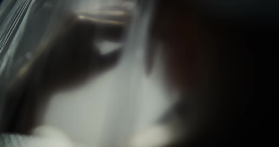 A woman touches herself under a translucent plastic bag in front of a dark background