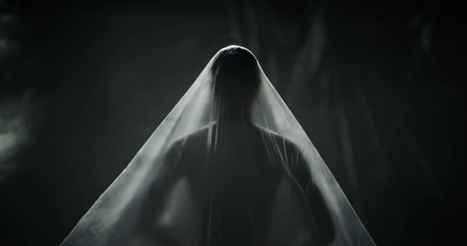 A nude woman is standing under sheer fabric and she raises her arms and puts them down then raises her arms over her head