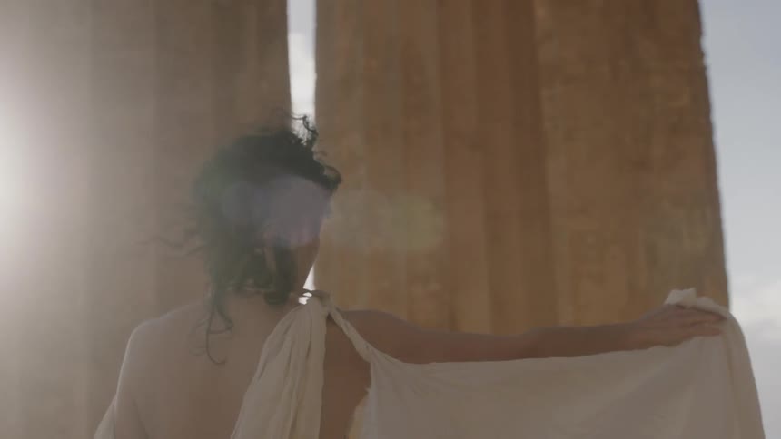 A woman walking through the acropolis as the wind causes her dress train to billow