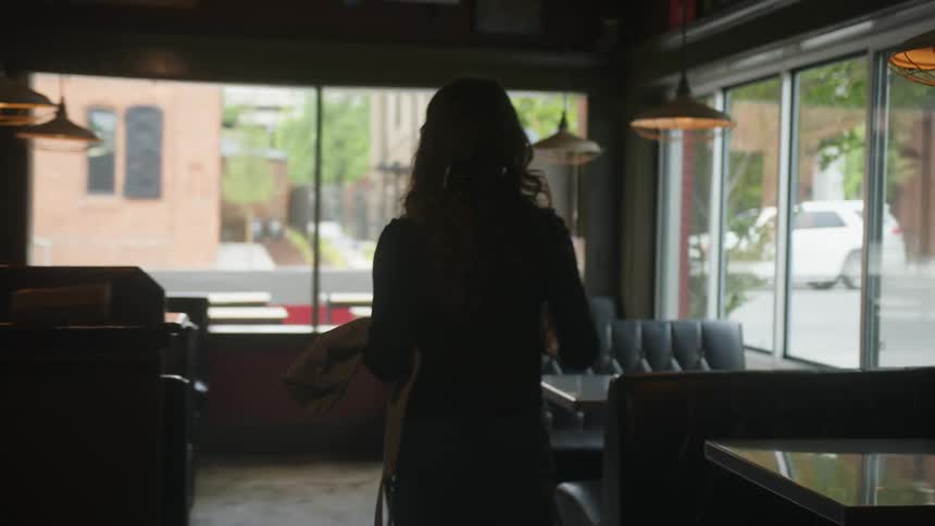 A woman in a restaurant walks towards a table and sets a cup of coffee down
