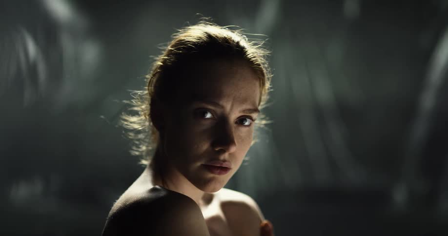 Nude woman with brown hair looks over her right shoulder and stares at camera in studio