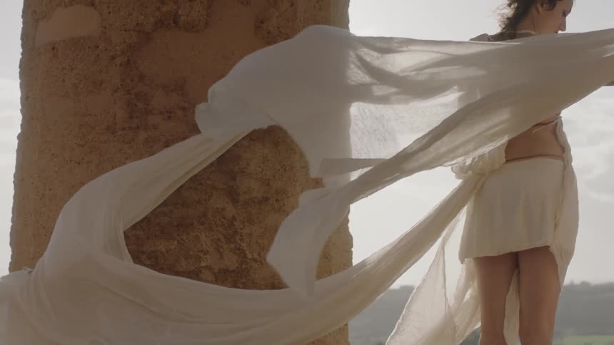 A woman in a flowing white dress stands near a pillar