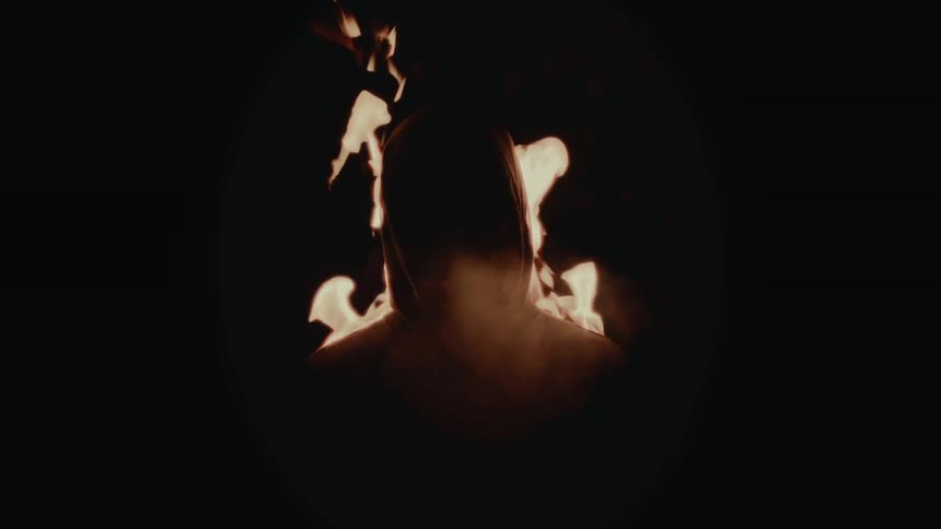 Silhouette of the head and shoulders of a person surrounded by flames and smoke in the dark