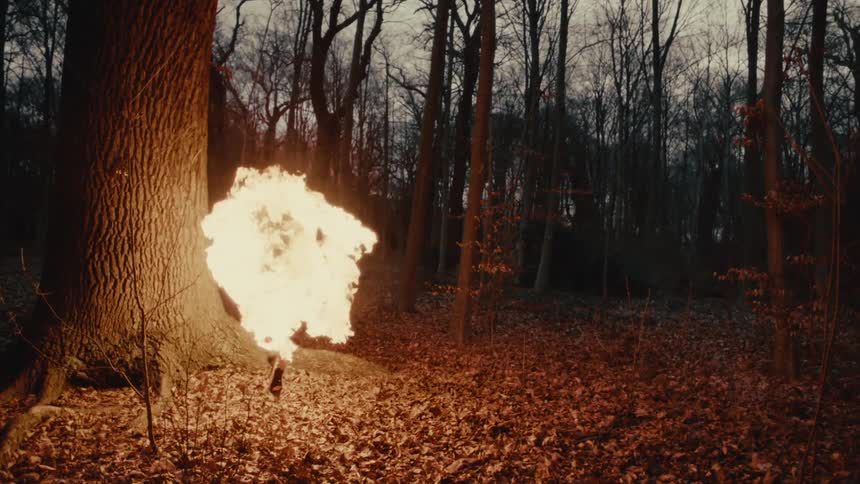 A person is on fire as they run through a forest and leap over tree roots leaving a trail of flames behind them