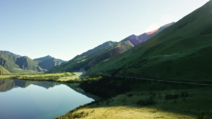 A reflective blue mirror lake surrounded by hills with lens flare