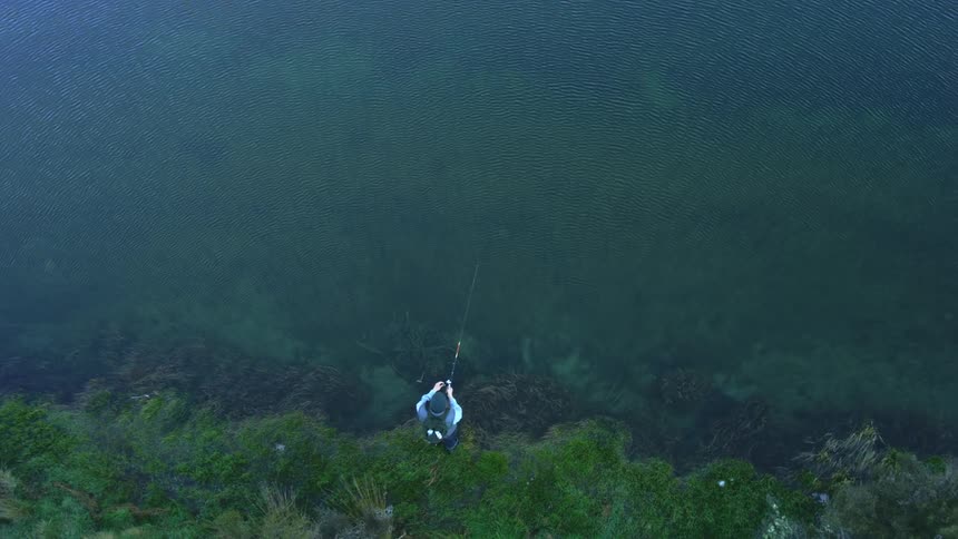 A fisherman casts a fishing line into a calm lake